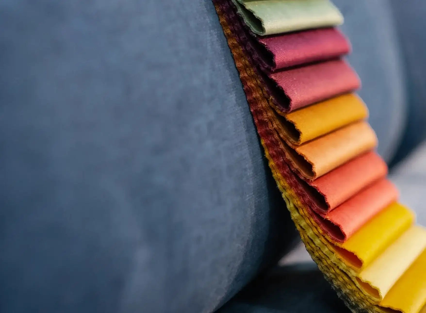 A stack of colorful, textured fabric swatches arranged in a gradient from deep red to bright yellow.