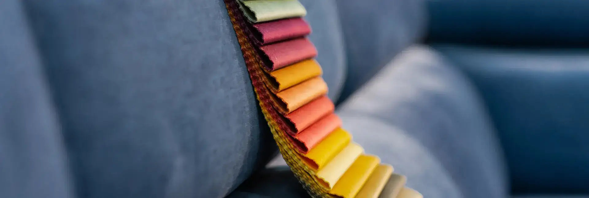A vibrant, rainbow-colored fabric swatch roll with a woven border rests against a soft blue upholstered surface.